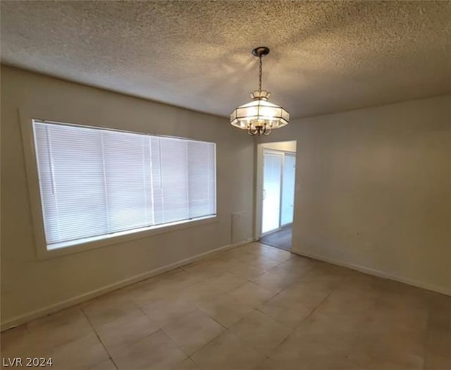 tiled spare room featuring a notable chandelier and a textured ceiling