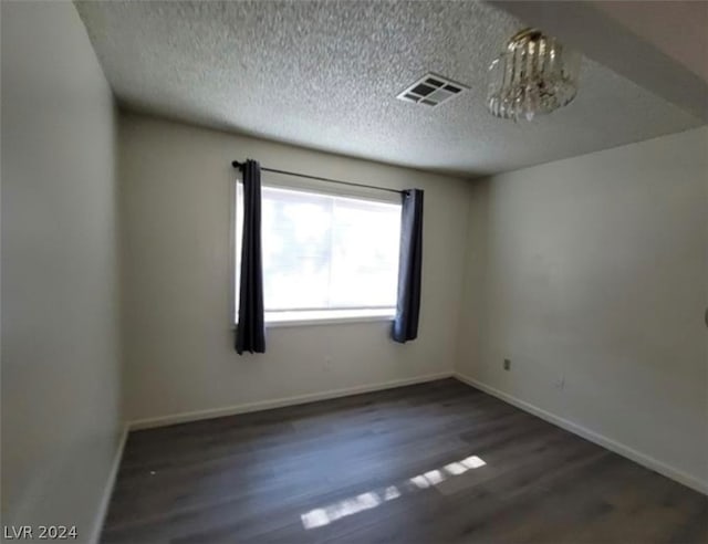 spare room featuring an inviting chandelier, dark hardwood / wood-style flooring, and a textured ceiling