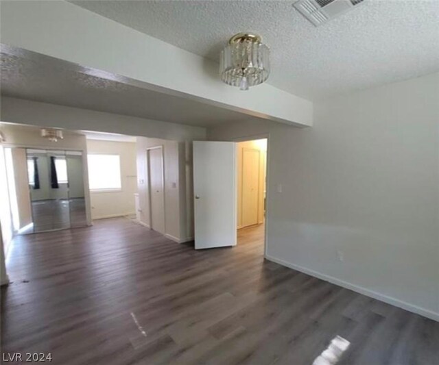 unfurnished living room with a notable chandelier, dark wood-type flooring, and a textured ceiling