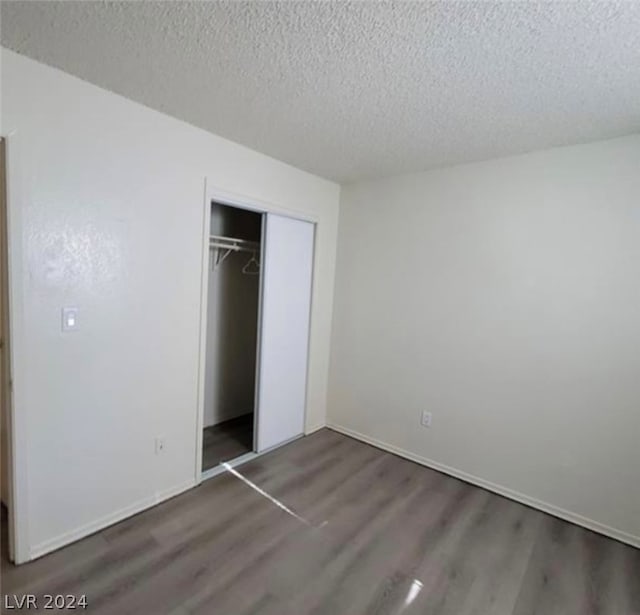 unfurnished bedroom featuring a textured ceiling, dark hardwood / wood-style floors, and a closet