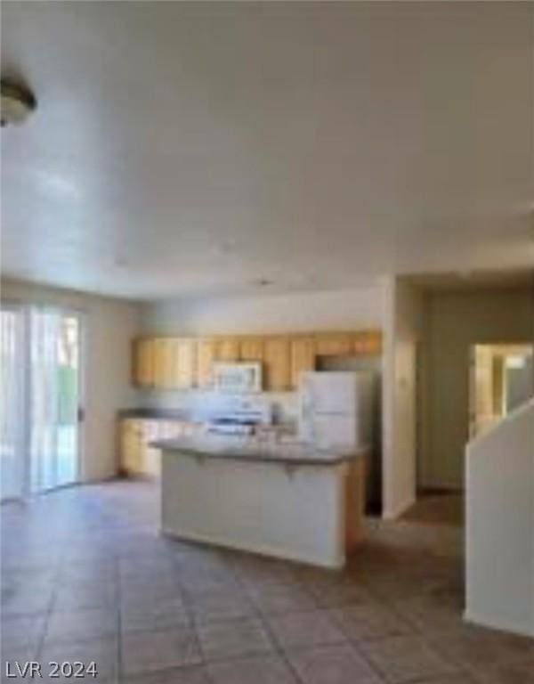 kitchen with white appliances, light tile patterned floors, an island with sink, and light brown cabinets