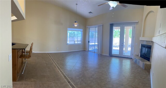 unfurnished living room with a fireplace, ceiling fan, tile floors, high vaulted ceiling, and french doors