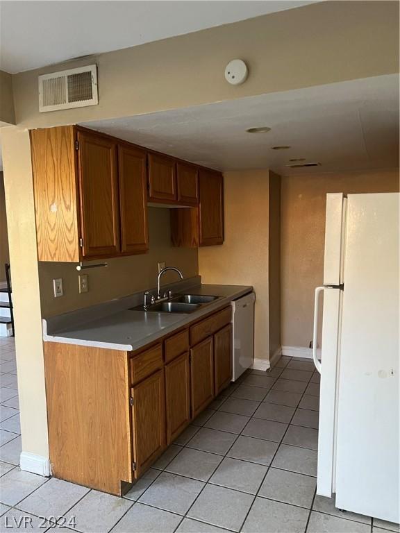 kitchen with white appliances, visible vents, brown cabinets, light countertops, and a sink