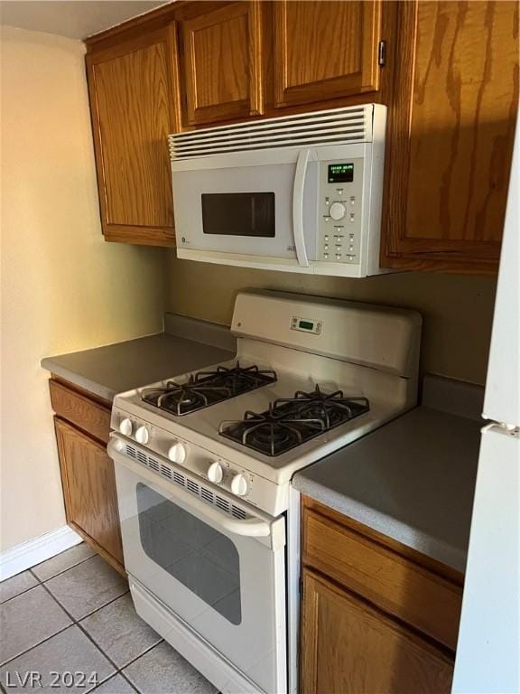 kitchen featuring white appliances, light tile patterned floors, baseboards, and brown cabinetry