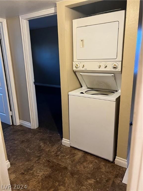 clothes washing area featuring stacked washer and clothes dryer, baseboards, and laundry area