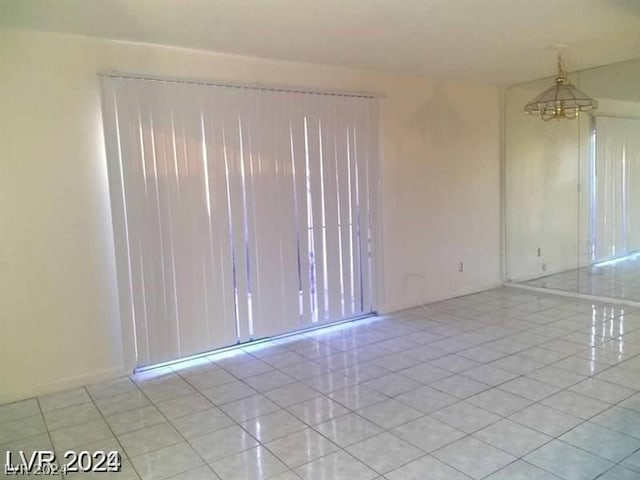 empty room with light tile patterned floors and an inviting chandelier