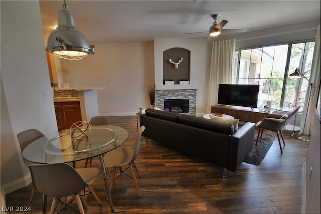 living room with a stone fireplace, dark hardwood / wood-style floors, and ceiling fan