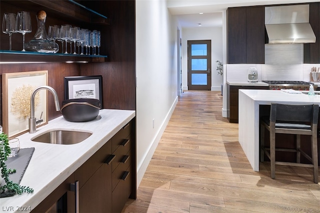 kitchen featuring light hardwood / wood-style floors, wall chimney exhaust hood, tasteful backsplash, sink, and dark brown cabinets