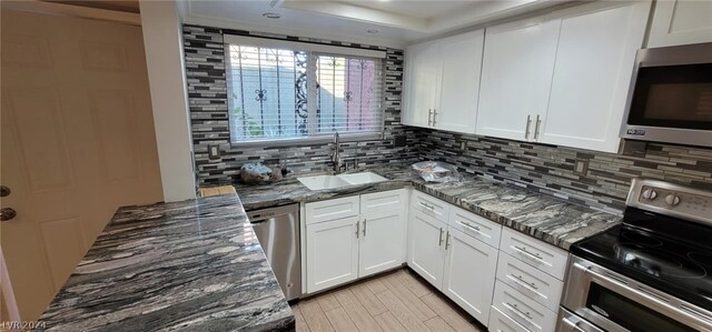 kitchen with white cabinetry, dark stone countertops, backsplash, stainless steel appliances, and sink