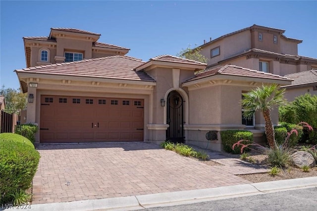 mediterranean / spanish-style house featuring a garage, decorative driveway, a tile roof, and stucco siding