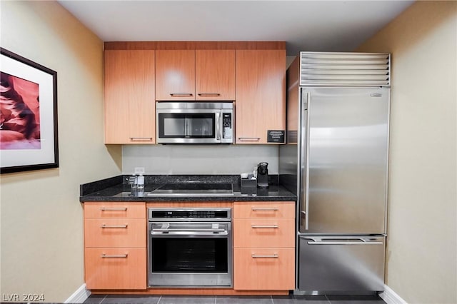 kitchen featuring dark tile patterned floors, dark stone counters, and appliances with stainless steel finishes