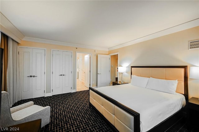 bedroom featuring carpet flooring, two closets, ornamental molding, and ensuite bathroom