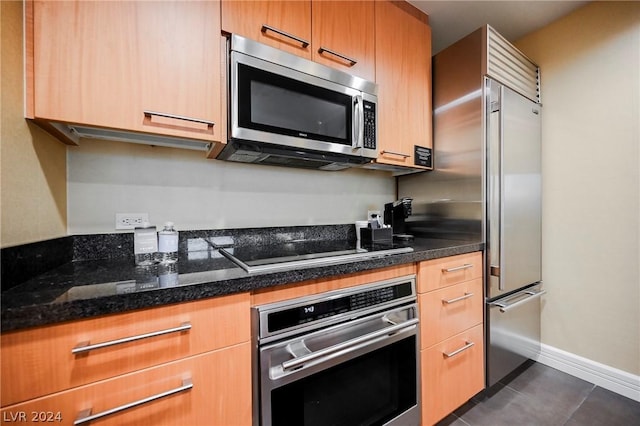 kitchen featuring stainless steel appliances, dark tile patterned flooring, and dark stone countertops