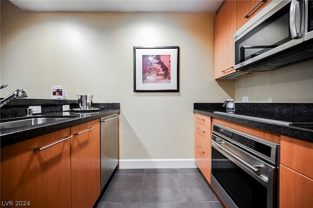 kitchen featuring stainless steel appliances, dark tile patterned flooring, dark stone countertops, and sink