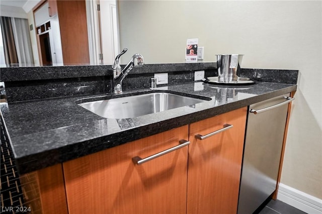 kitchen with stainless steel dishwasher, sink, dark stone counters, and tile patterned floors