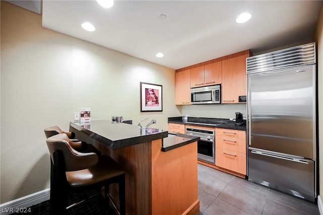 kitchen featuring a kitchen bar, kitchen peninsula, stainless steel appliances, sink, and light tile patterned flooring