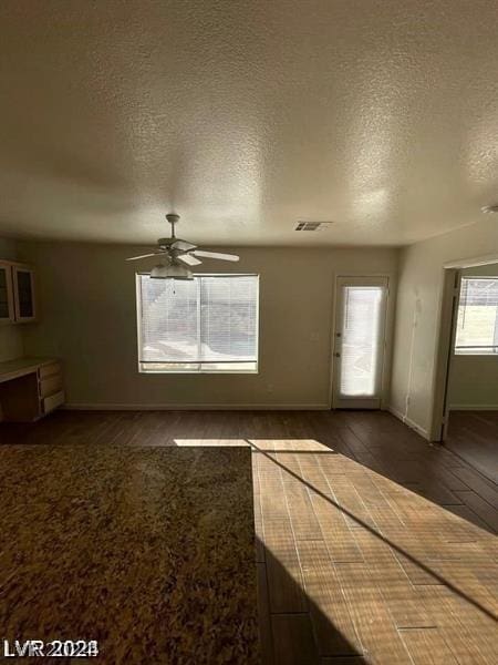 unfurnished living room with ceiling fan, dark wood-type flooring, and a textured ceiling