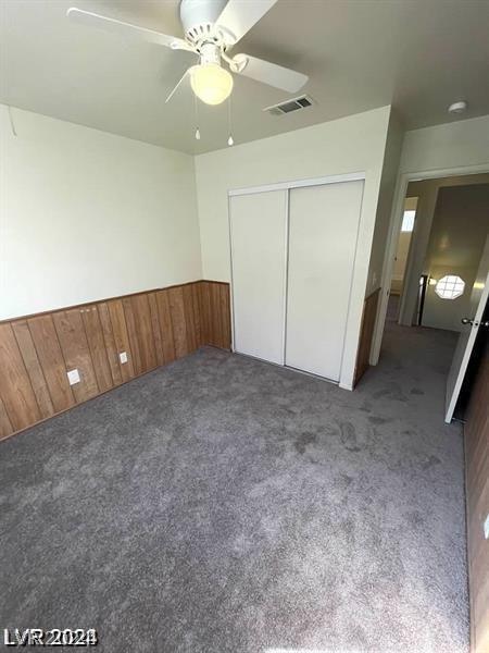 unfurnished bedroom featuring a closet, carpet, wooden walls, and ceiling fan