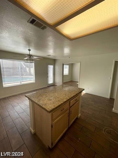 kitchen with ceiling fan, a wealth of natural light, light stone counters, and a kitchen island