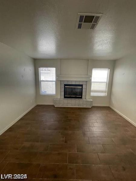 unfurnished living room featuring a textured ceiling, a tile fireplace, and a healthy amount of sunlight