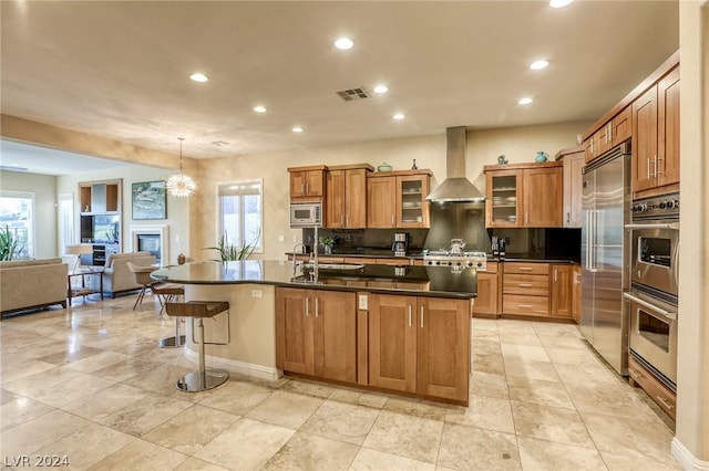 kitchen featuring a center island with sink, wall chimney exhaust hood, pendant lighting, and built in appliances