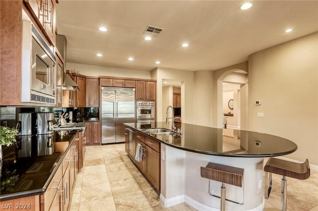 kitchen with built in appliances, decorative backsplash, sink, and an island with sink