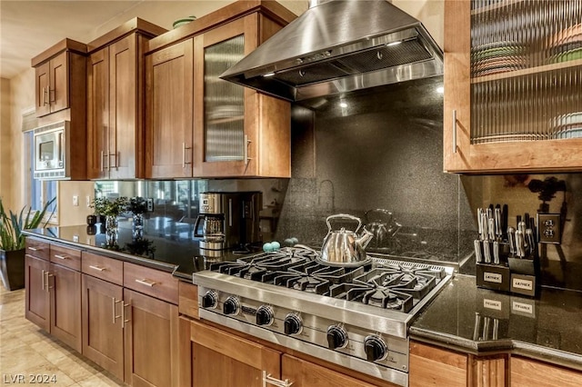 kitchen with dark stone countertops, wall chimney range hood, appliances with stainless steel finishes, and tasteful backsplash