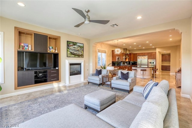 living room with built in features and ceiling fan with notable chandelier