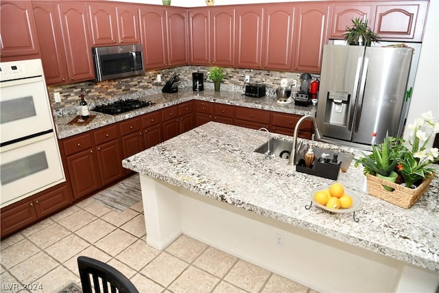 kitchen featuring tasteful backsplash, appliances with stainless steel finishes, light stone countertops, and light tile patterned floors