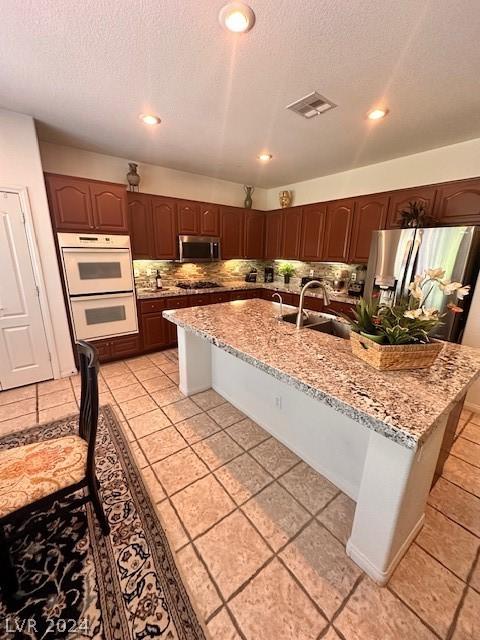 kitchen with sink, backsplash, an island with sink, and appliances with stainless steel finishes