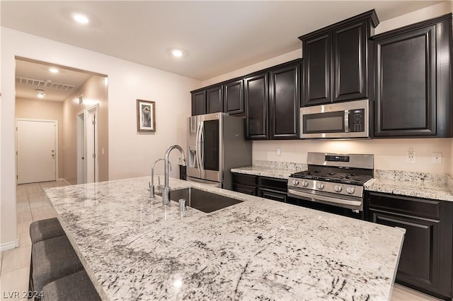 kitchen with a kitchen bar, appliances with stainless steel finishes, light stone counters, sink, and a center island with sink