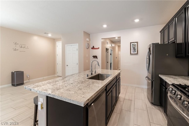 kitchen with appliances with stainless steel finishes, a kitchen breakfast bar, light stone counters, sink, and an island with sink