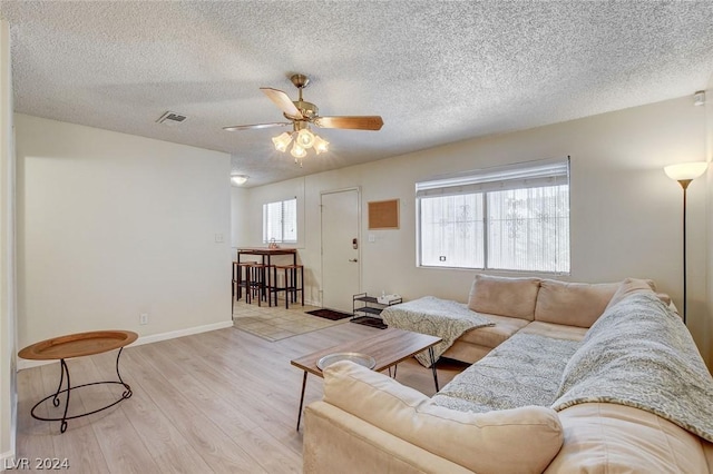 living room with ceiling fan, a textured ceiling, and light wood-type flooring