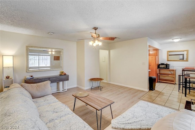 living room with a textured ceiling, ceiling fan, and light hardwood / wood-style flooring