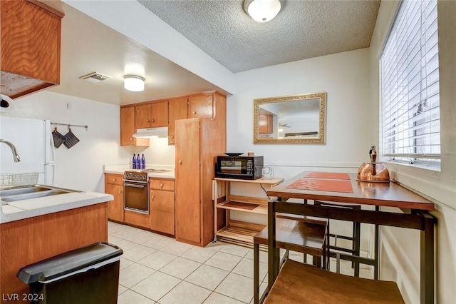 kitchen featuring light tile patterned flooring, stainless steel stove, sink, and a textured ceiling