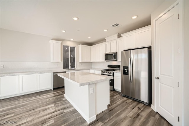 kitchen featuring appliances with stainless steel finishes, white cabinets, a center island, and light stone counters