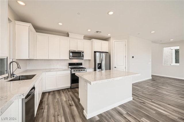 kitchen featuring light stone counters, a center island, white cabinetry, appliances with stainless steel finishes, and sink