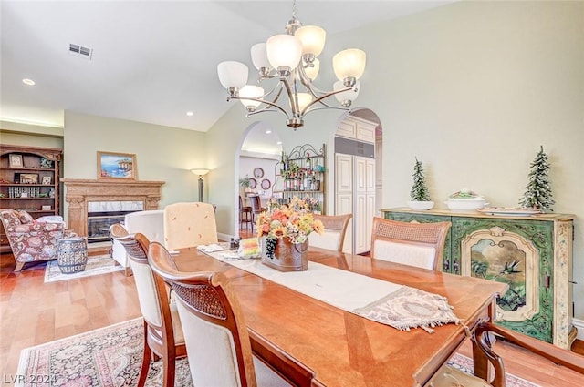 dining room with built in features, vaulted ceiling, light hardwood / wood-style floors, and an inviting chandelier