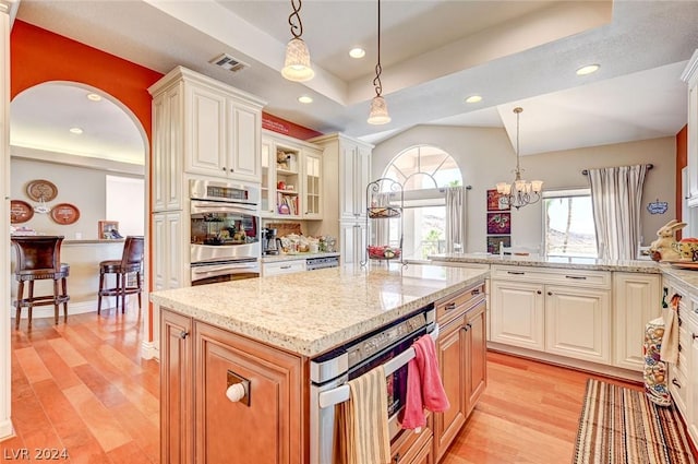 kitchen featuring a raised ceiling, a notable chandelier, double oven, pendant lighting, and a kitchen island