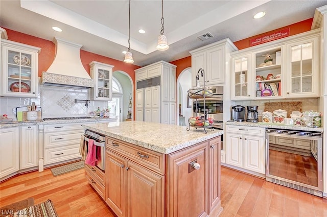 kitchen with custom exhaust hood, a center island, backsplash, a raised ceiling, and white cabinetry