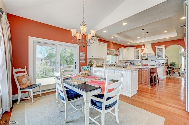 dining area with a tray ceiling, sink, light wood-type flooring, and a notable chandelier