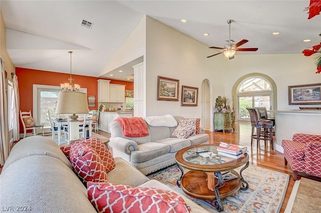 living room featuring light wood-type flooring, ceiling fan with notable chandelier, high vaulted ceiling, and a healthy amount of sunlight