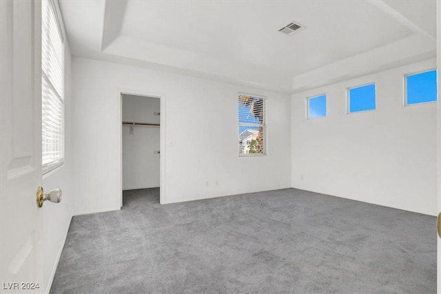 unfurnished bedroom featuring a closet, a spacious closet, a tray ceiling, and dark carpet