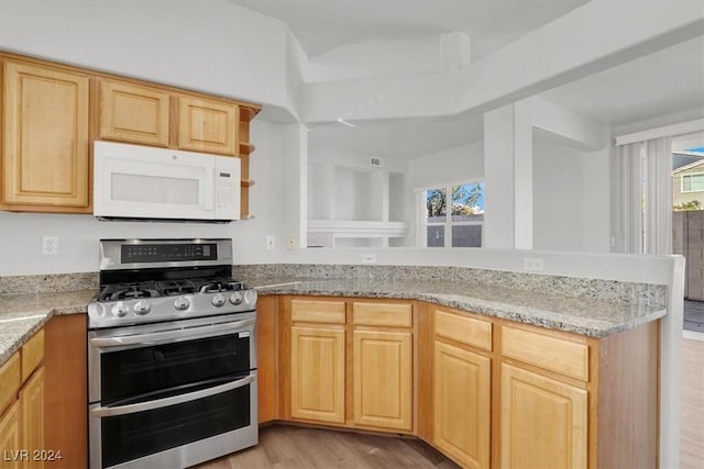 kitchen featuring kitchen peninsula, range with two ovens, light brown cabinetry, light hardwood / wood-style flooring, and light stone counters