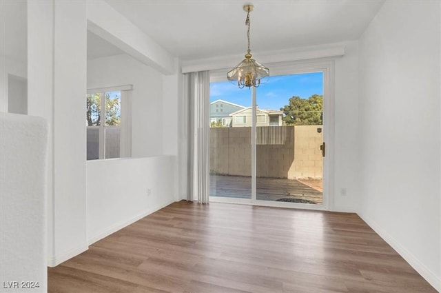 unfurnished dining area with wood-type flooring, an inviting chandelier, and a healthy amount of sunlight