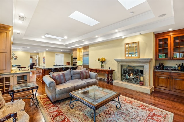 living room featuring dark wood-type flooring, a skylight, a fireplace, and a raised ceiling