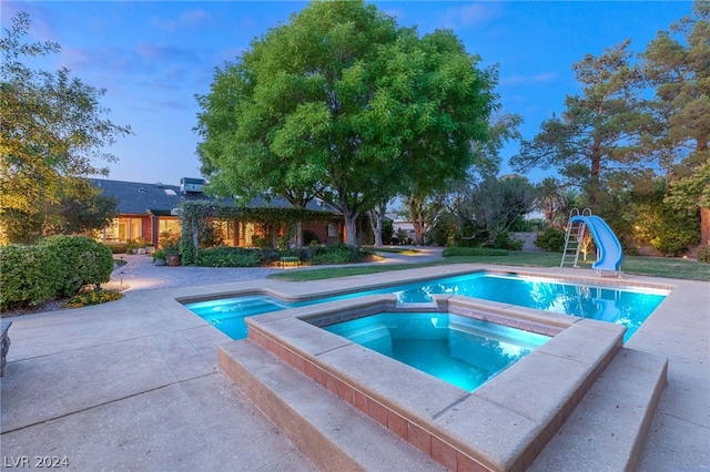 pool at dusk with an in ground hot tub and a water slide