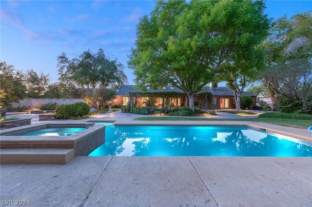 pool at dusk with an in ground hot tub