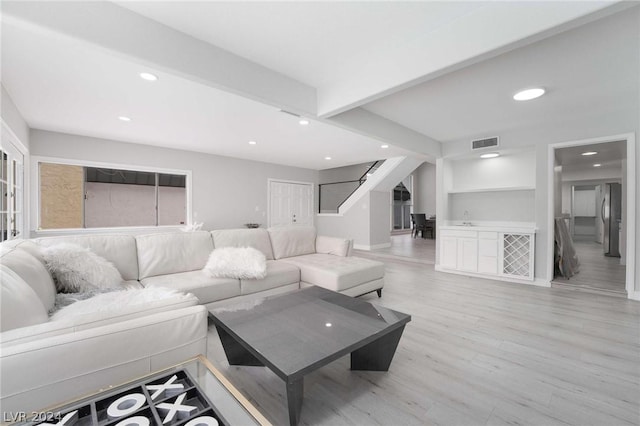 living room with built in shelves, sink, beam ceiling, and light hardwood / wood-style floors