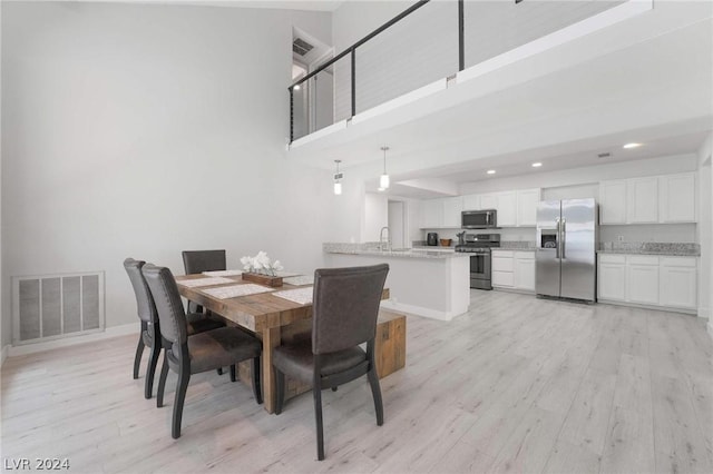 dining room with sink, a towering ceiling, and light wood-type flooring